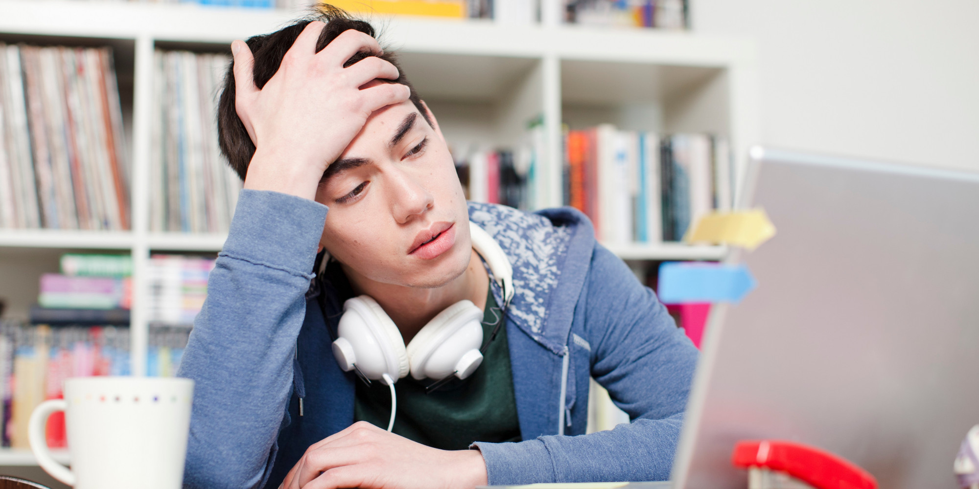 Worried male student with hand in hair using laptop